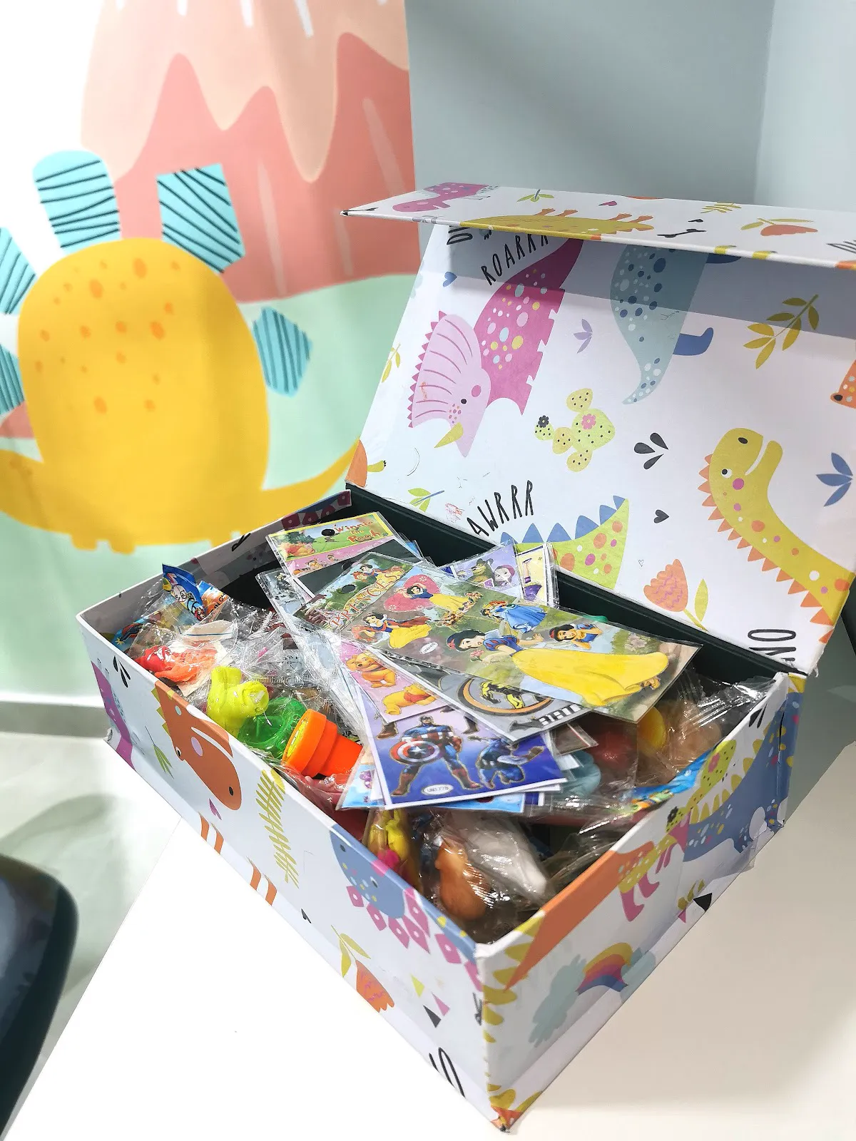 A caixa mágica aberta, cheia de brinquedos e presentes, diante da parede pintada.